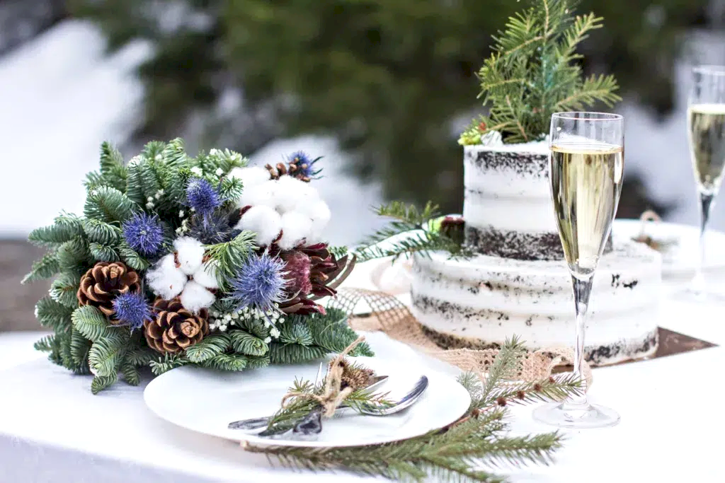 Aerial view of winter green garland on a wedding table with white plates, cake, glasses, champagne.