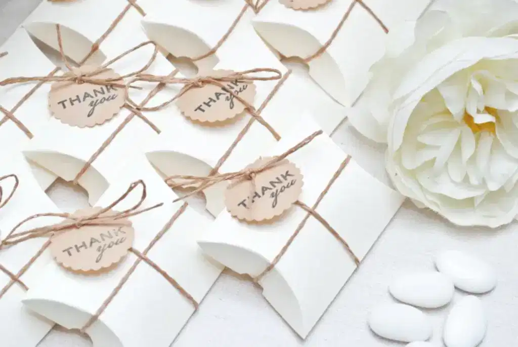 Wedding favors lying in a row on a white table with a white flower to the right.